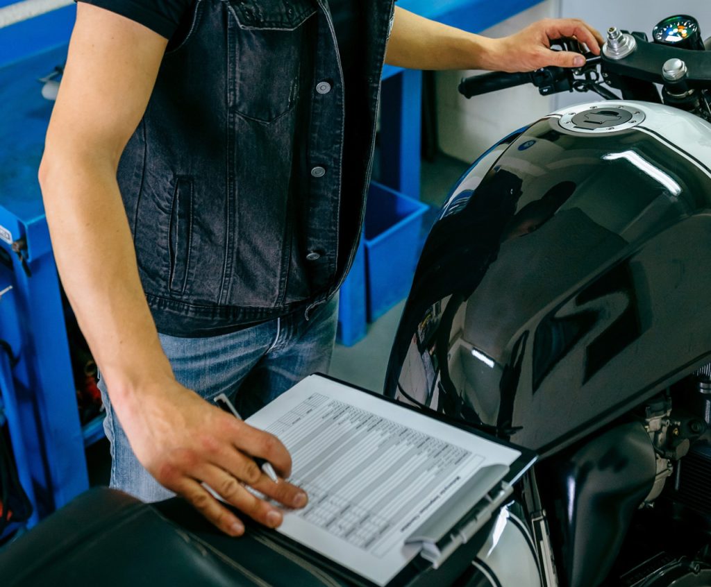 Close up of a detailed motorcycle inspection Houston checklist being completed by a mechanic in a service garage.