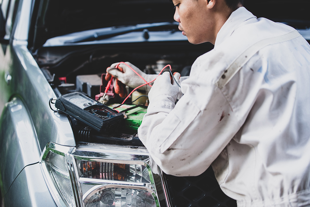 Professional Mercedes Benz inspection using a digital multimeter to test car battery voltage and electrical systems.
