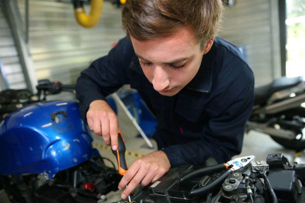 Expert motorcycle inspection Houston mechanic using a screwdriver for a detailed engine tune-up and maintenance.