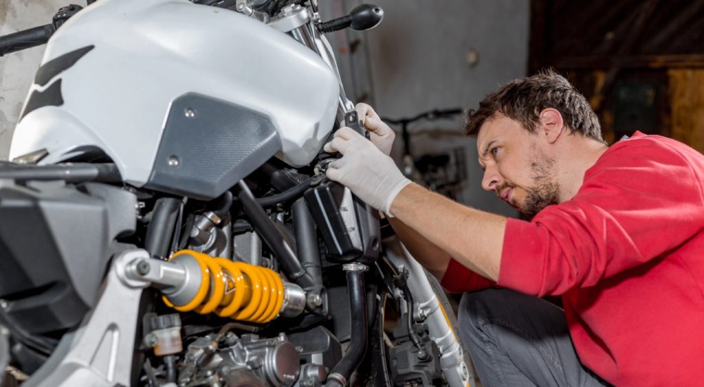 Professional motorcycle inspection Houston technician checking coolant levels and yellow rear suspension coil.