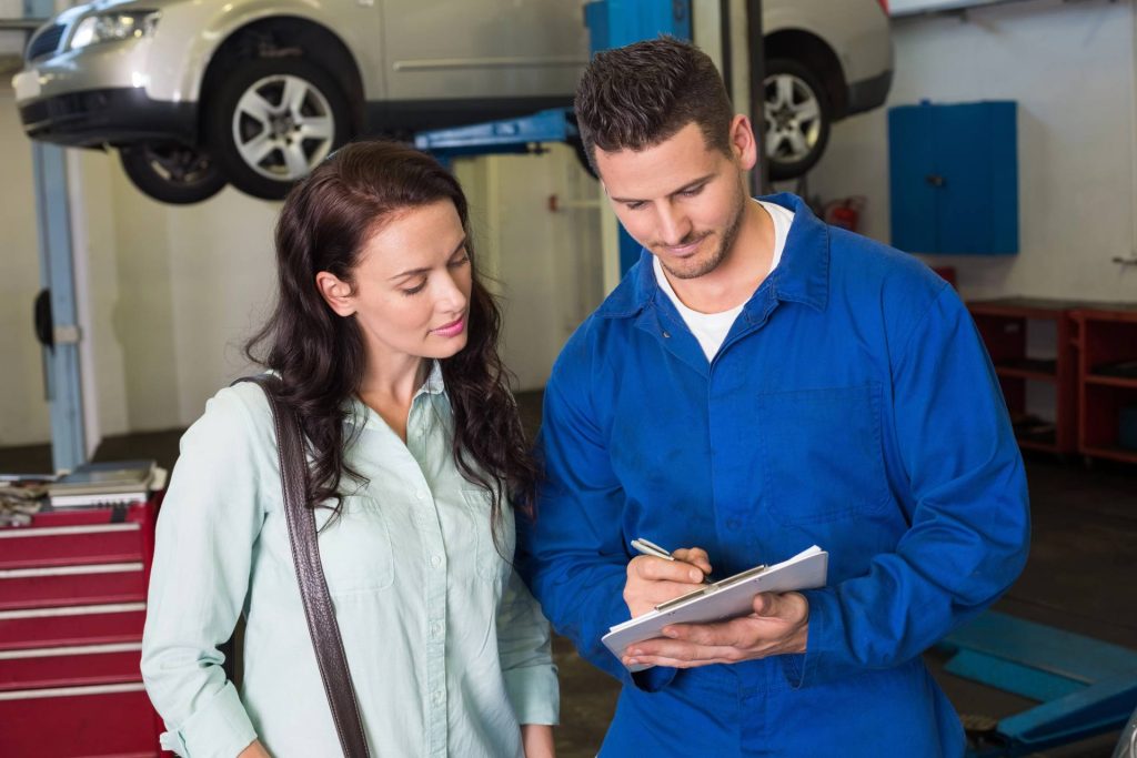 Mechanic showing a third party inspection report to a female customer in a professional automotive repair garage.