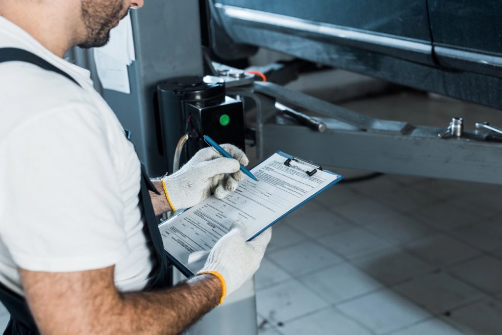 Professional technician filling out a used car check Houston diagnostic form while inspecting a vehicle on a lift.