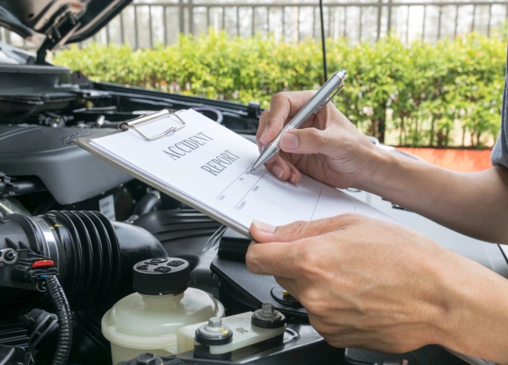 Inspector filing an accident report during a certified pre owned car inspection service to verify vehicle history records.