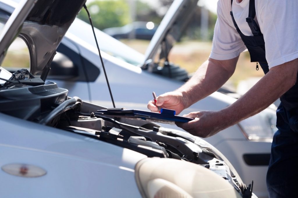 Mechanic performing a multi-point check for a certified pre owned car inspection service on a fleet of used sedan vehicles.