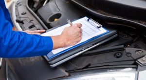 Professional technician filling out a detailed report for an independent used car inspection on a vehicle.