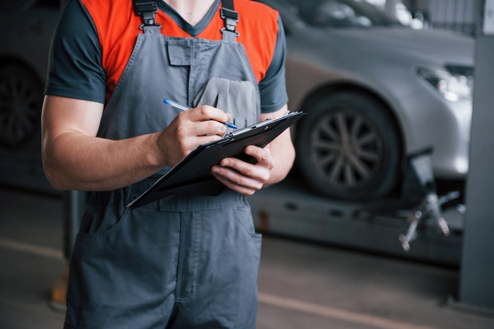 Mechanic in grey and red overalls writes on a clipboard to document a detailed third party inspection Houston.