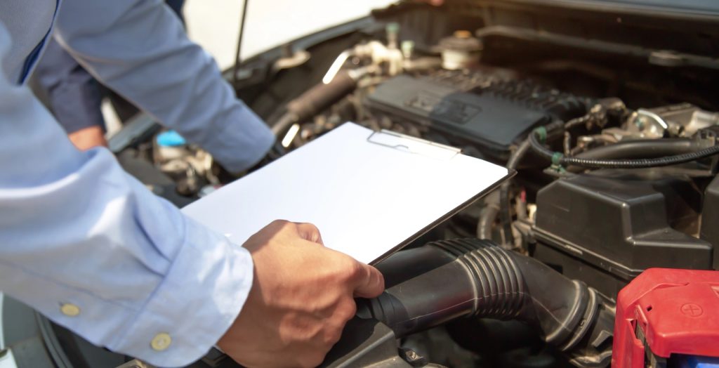 A specialist holds a clipboard over an open engine bay during a detailed pre purchase used car inspection process.