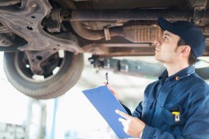 A mechanic at an auto shop looking up while documenting findings on a blue clipboard for a pre purchase inspection Houston.