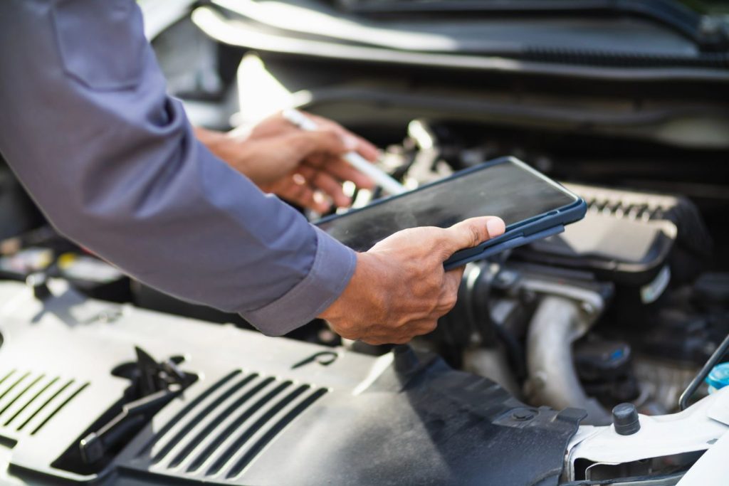 Expert mechanic to check used car before buying using a digital tablet for a detailed engine bay safety inspection. 