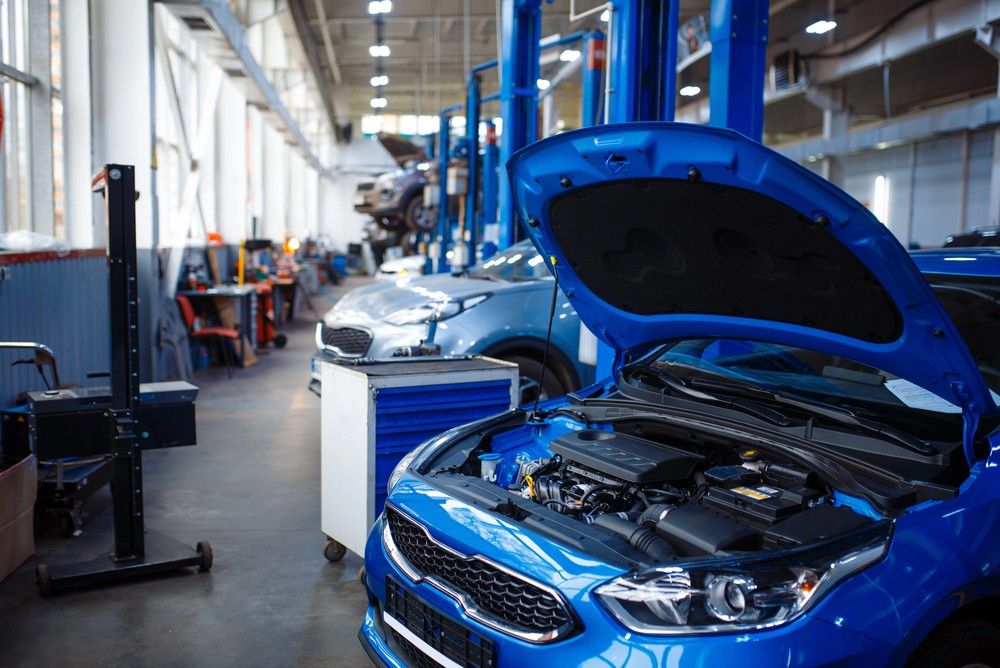 Interior of a busy auto repair shop with several lifts, showing a blue car with its hood open for a pre purchase inspection Houston.