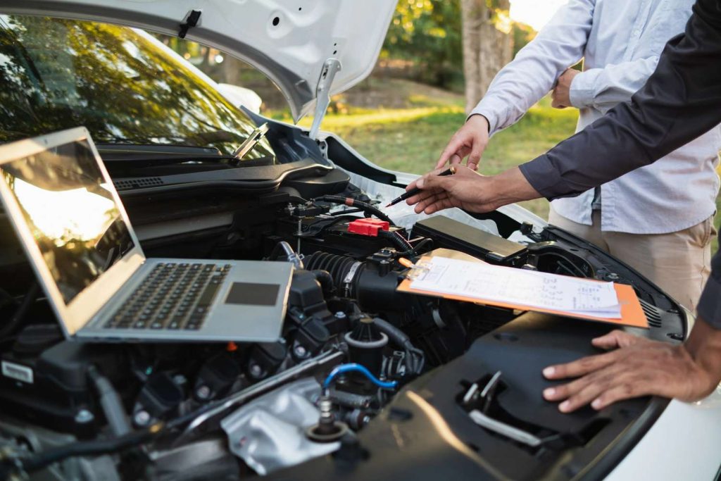 Professional mechanic to check used car before buying using laptop diagnostics and inspection paperwork on engine. 