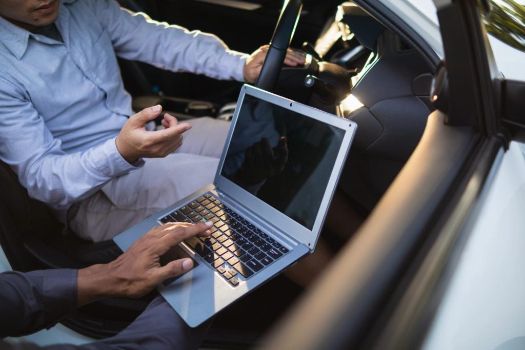 Skilled mechanic to check used car before buying while performing an onboard computer diagnostic in the car interior.