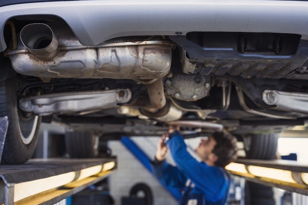 Low-angle shot of a car’s exhaust system, muffler, and suspension during a thorough pre purchase inspection Houston at a shop.