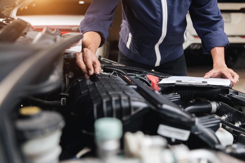 A certified mobile mechanic points at an engine component during a comprehensive used car inspection under the hood.