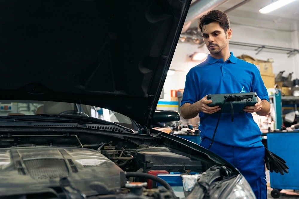 A certified mobile mechanic stands by an open car hood and checks systems using professional diagnostic tools for an inspection.