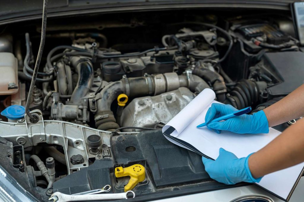 Certified mobile mechanic used car inspection filling out a detailed maintenance checklist over the engine.