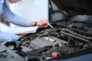 Professional certified mobile mechanic used car inspection examining the engine bay components with a pen.