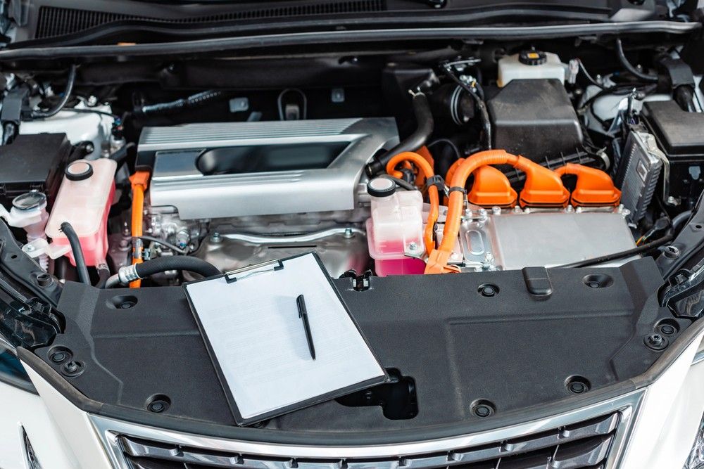 A clipboard and pen rest on the open engine bay of a modern hybrid car, ready for a detailed Pre purchase vehicle inspection Houston.