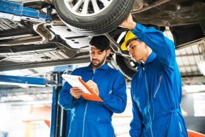 Experts performing a mobile third party car inspection service by checking the undercarriage on a professional lift.