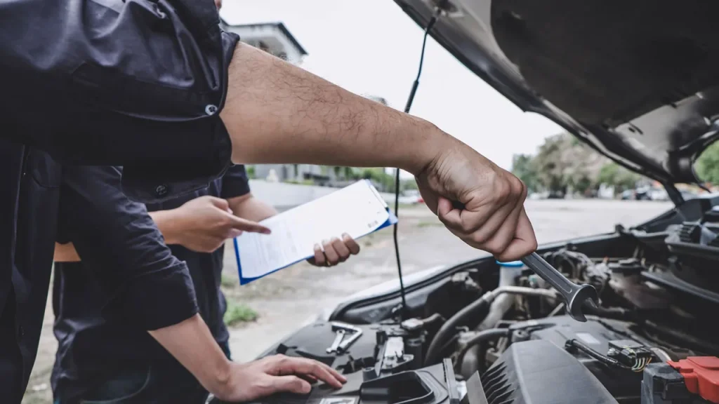 Mechanics using a wrench and clipboard during a detailed pre purchase auto inspection service under the hood.