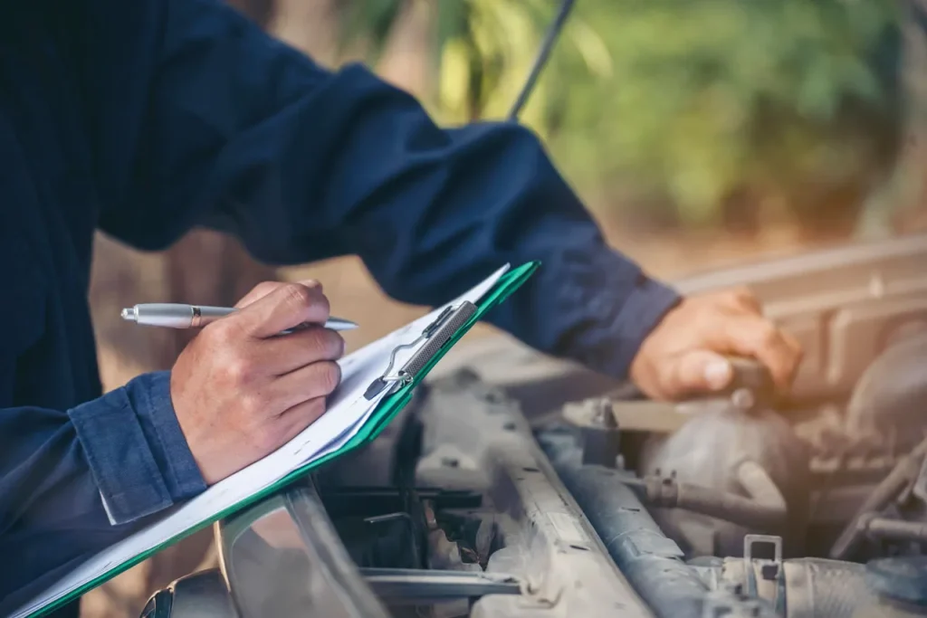 A mechanic filling out a checklist while performing a professional pre purchase auto inspection service on a car.