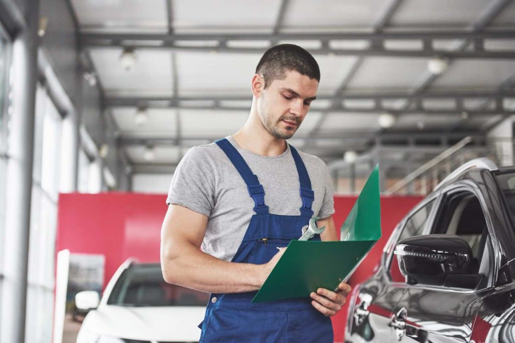 Auto technician reviewing a third party inspection green folder inside a professional car repair shop.