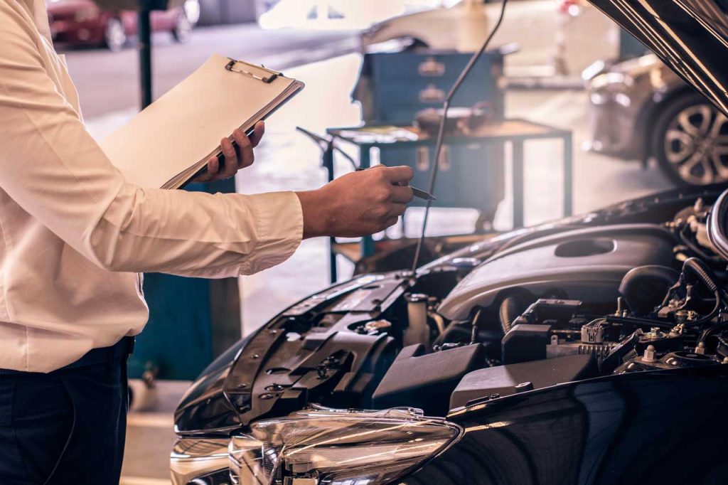 Mechanic with a clipboard to check used car service Houston options while inspecting a black vehicle engine.