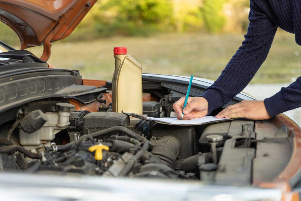 Technician signing a document to check used car service Houston maintenance and oil fluid levels under the hood.